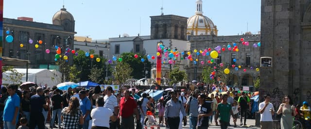 Lively plaza in Guadalajara's historic center with colorful balloons, cathedral dome in the background