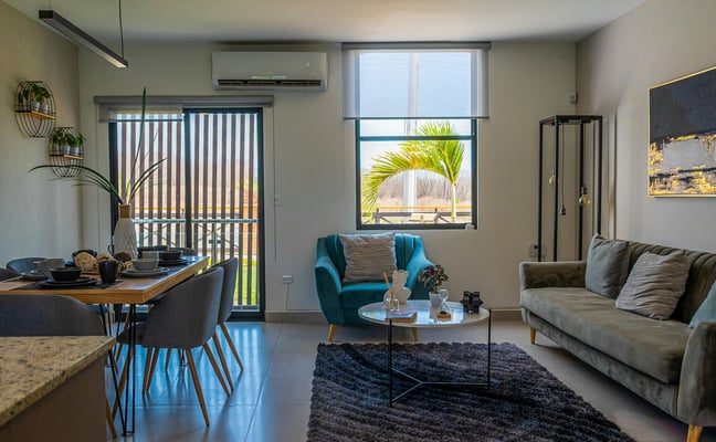 Modern open-plan apartment with teal armchair, dining area, and city light through large windows