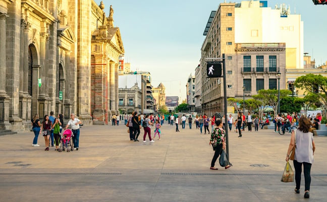 People walking through Guadalajara's historic plaza at golden hour, cathedral facade in the background
